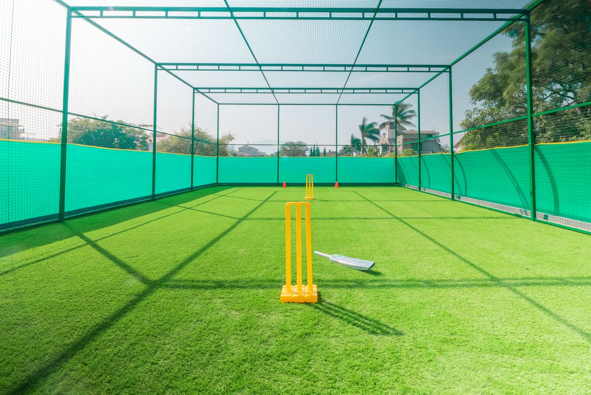 Outdoor cricket practice nets set up with bright yellow stumps
