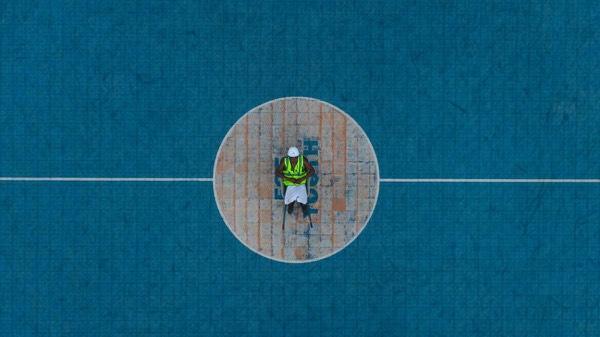 Construction worker in safety gear standing at the centre of a newly built sports court