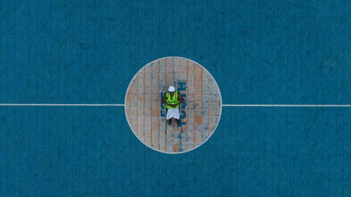 Construction worker in safety gear standing at the centre of a newly built sports court