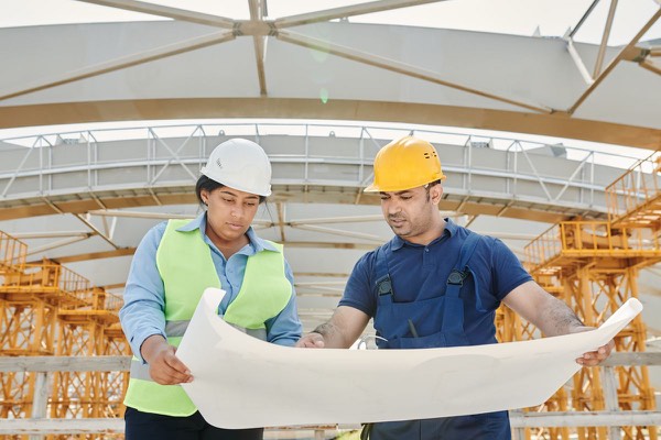 Engineers in safety helmets reviewing building plans together on site