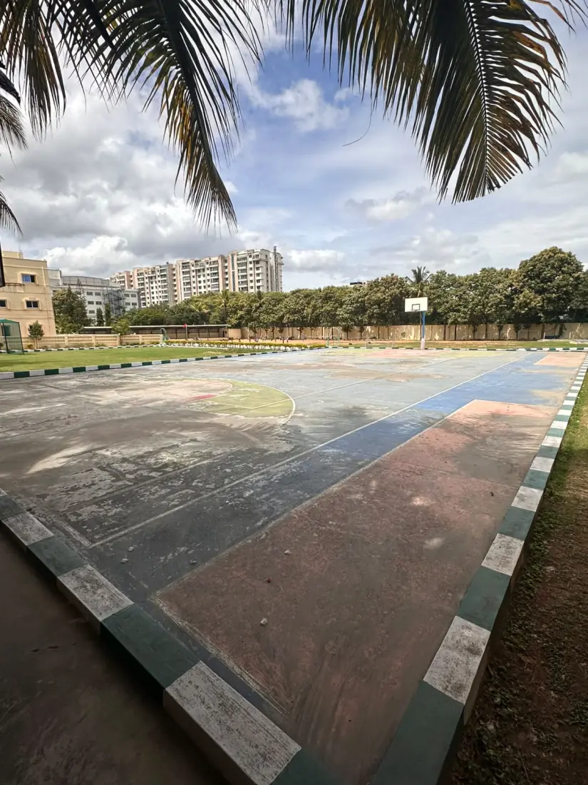 Worn concrete court at Anand Shiksha Kendra before resurfacing, with faded markings and patched repairs